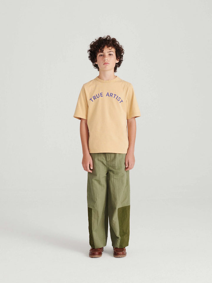 Garçon avec T shirt en coton caramel avec logo True Artist en bleu et pantalon vert