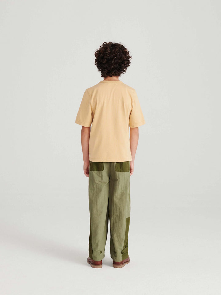 Garçon avec T shirt en coton caramel avec logo True Artist en bleu et pantalon vert