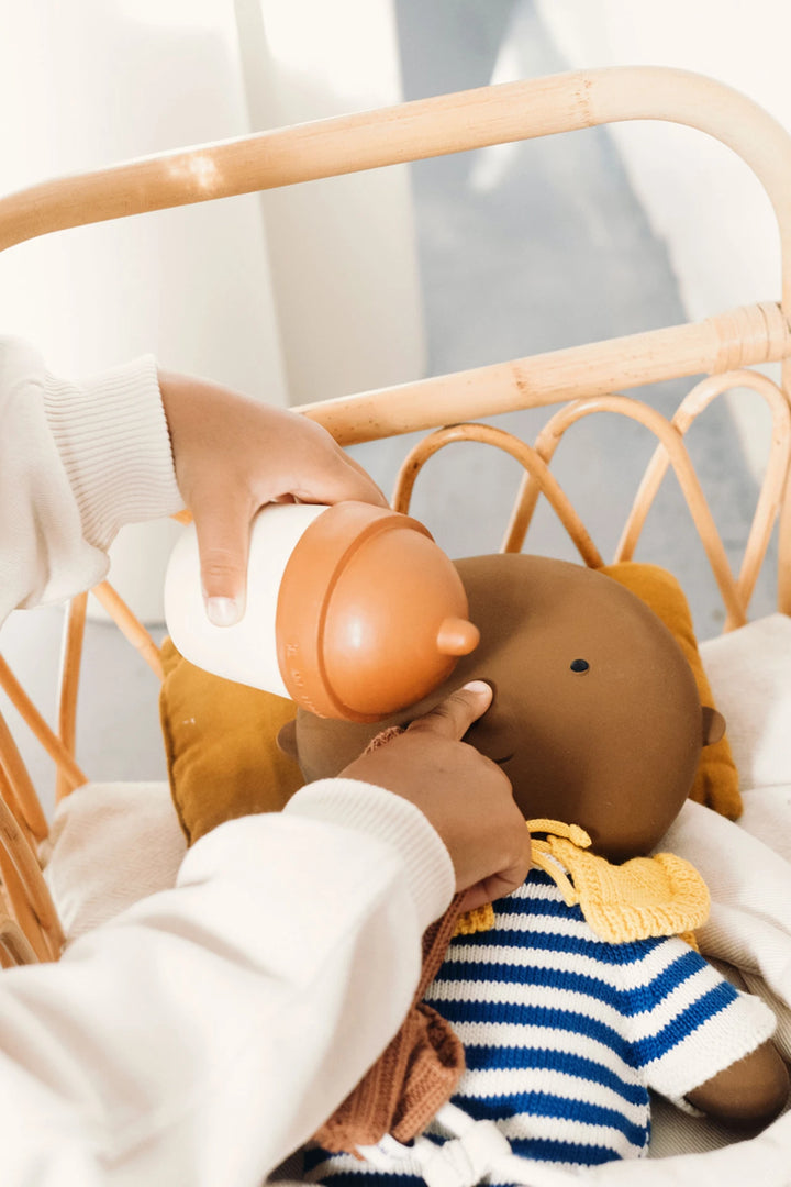 Main d'enfant avec Biberon Gommu beige et cannelle et poupée gommu