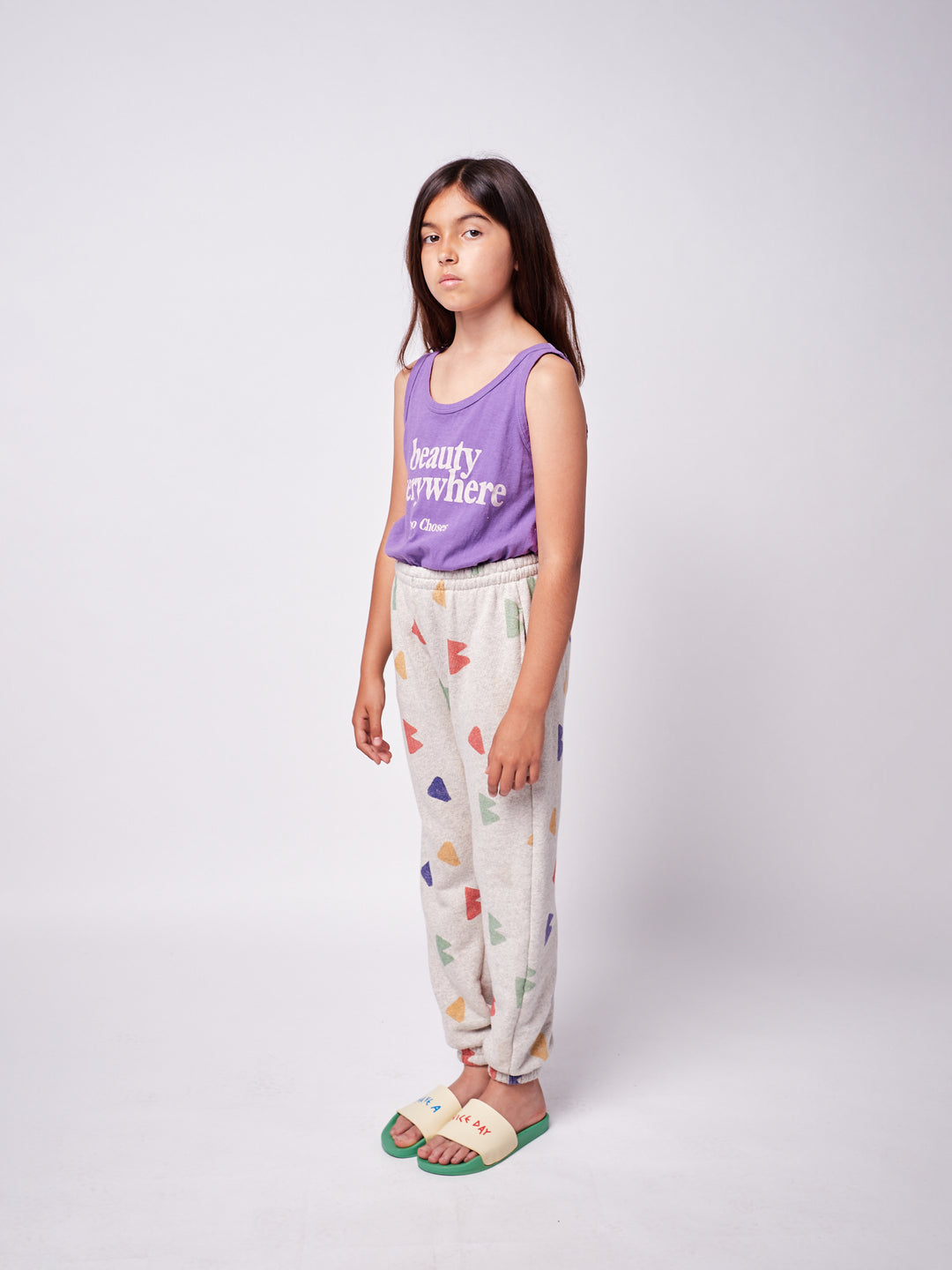 brown-haired little girl with purple bobo choses ''Beauty Everywhere'' playsuit and geometric multi-colored sweatpants