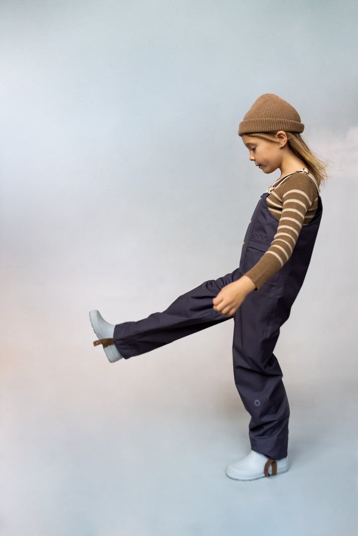 kid posing from the side wearing faire child rain dungarees in false indigo enfant posant de côté avec salopette de pluie faire child en bleu foncé