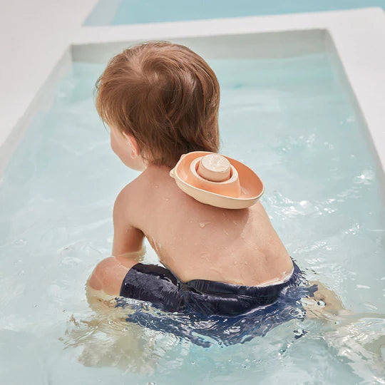 Enfant dans l'eau avec Bateau convertible en caoutchouc orange pastel Plan Toys
