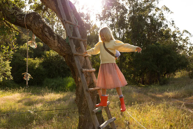 Fille qui monte sur un arbre avec des Bottes de pluie en caoutchouc orange 