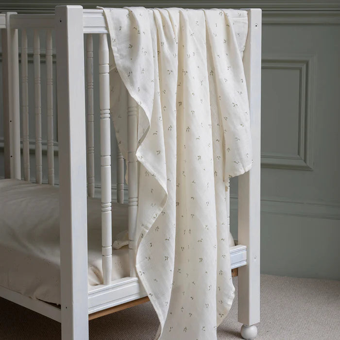 Couverture d'emmaillotage en coton blanc avec imprimé feuilles sur un lit de bébé