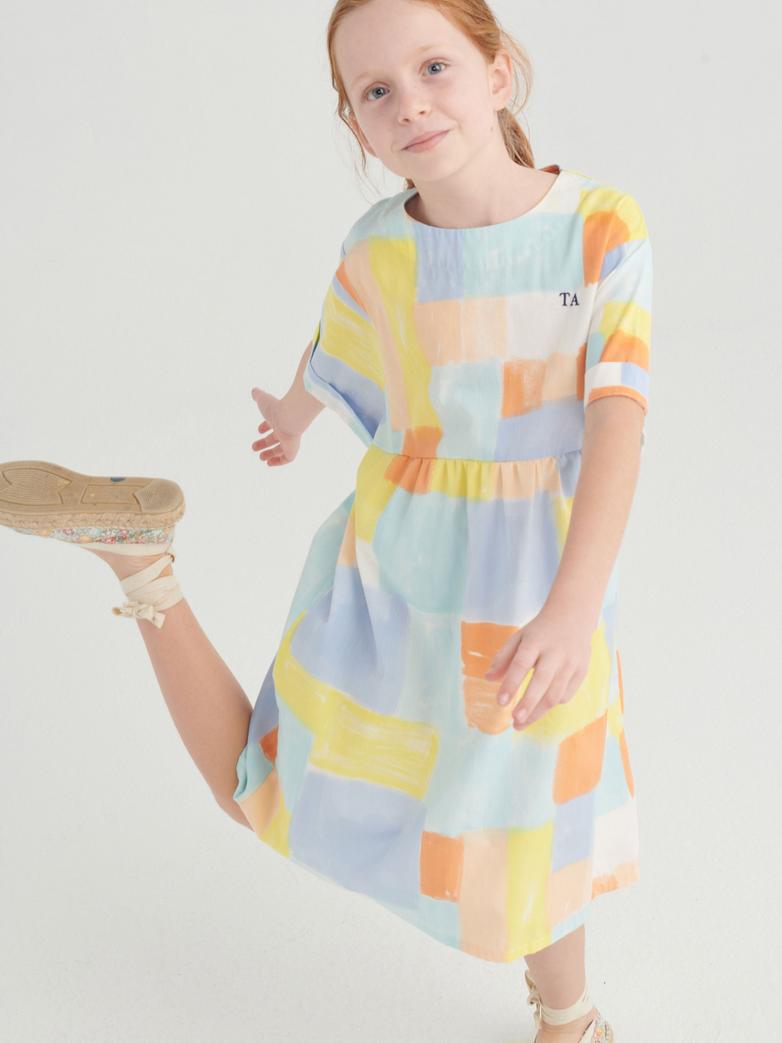 Fille avec Robe True Artist avec tissu coloré orange, jaune, bleu et blanc