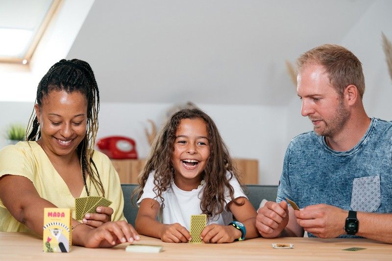 Deux Adultes et un enfant qui jouent le Jeu de poche Mada
