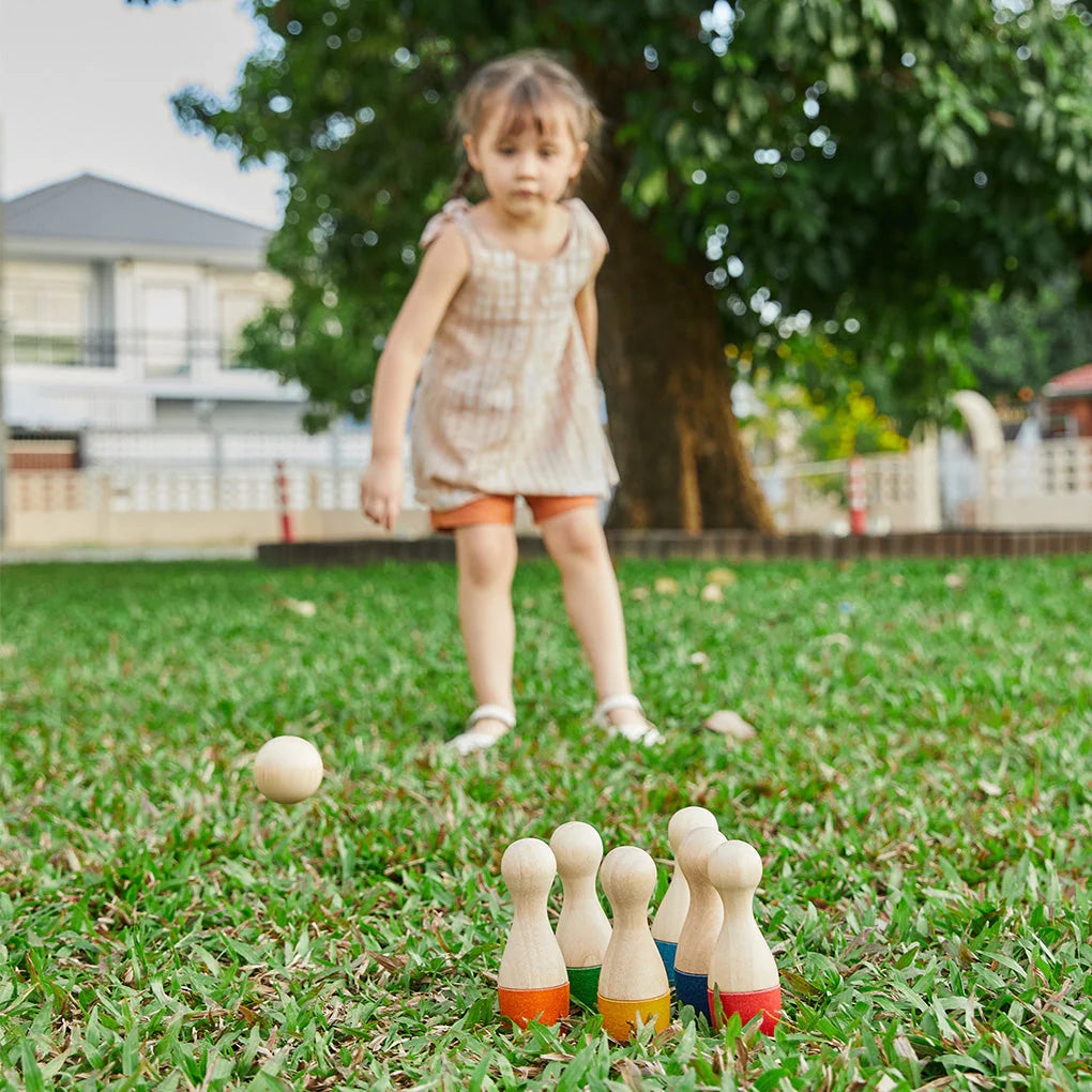 Enfant qui joue dans un jardin avec Jeu de quilles en bois Plan Toys