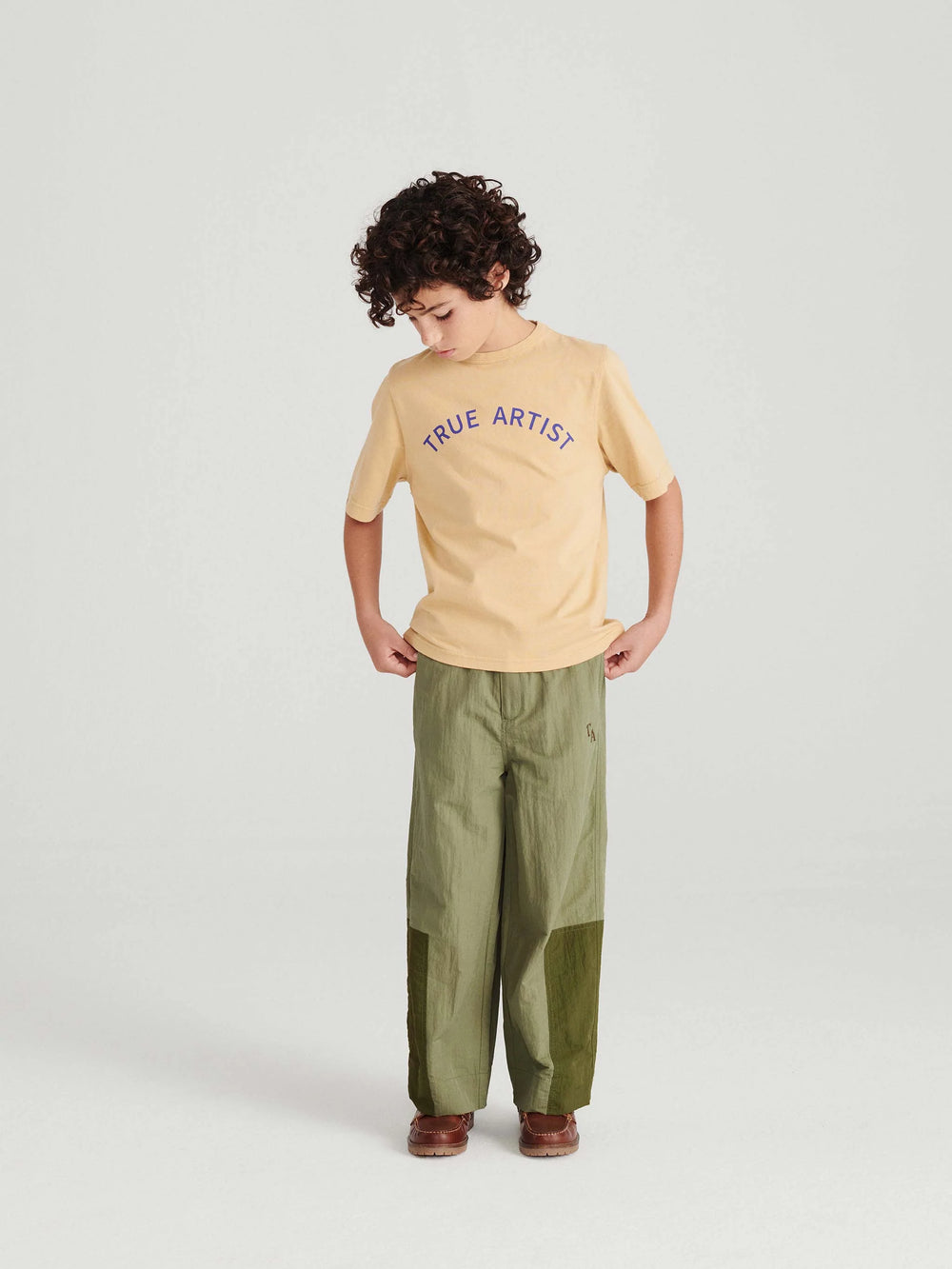 Garçon avec T shirt en coton caramel avec logo True Artist en bleu et pantalon vert