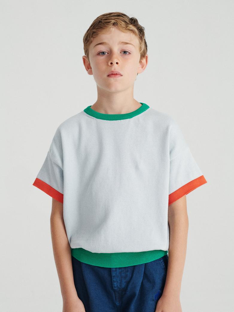 Garçon avec T-shirt True Artist tricoté en coton bleu pâle avec détails oranges et verts