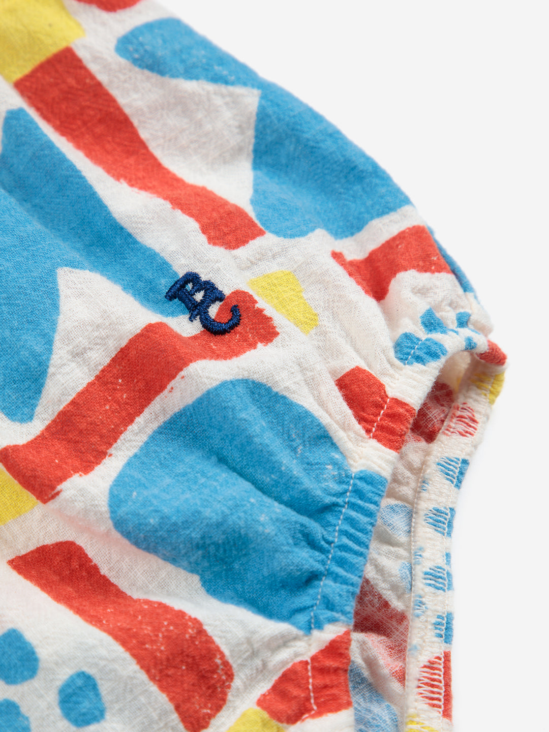 Détail d'Une-pièce pour bébé en coton blanc avec un motif géométrique bleu, rouge et jaune