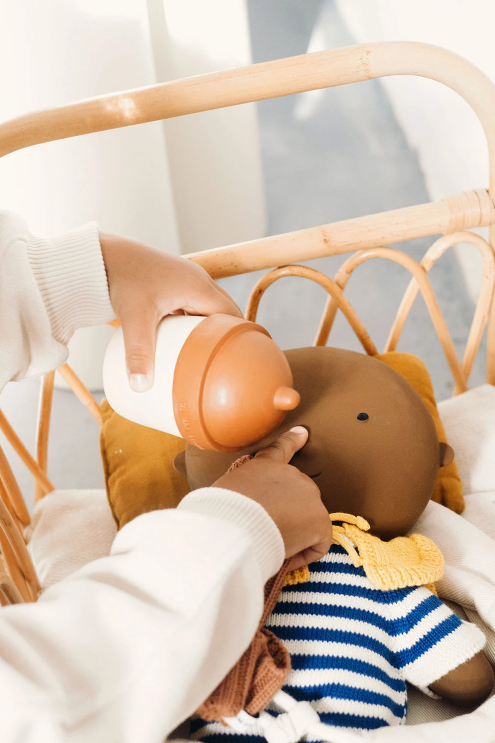 Main d'enfant avec Biberon Gommu beige et cannelle et poupée gommu
