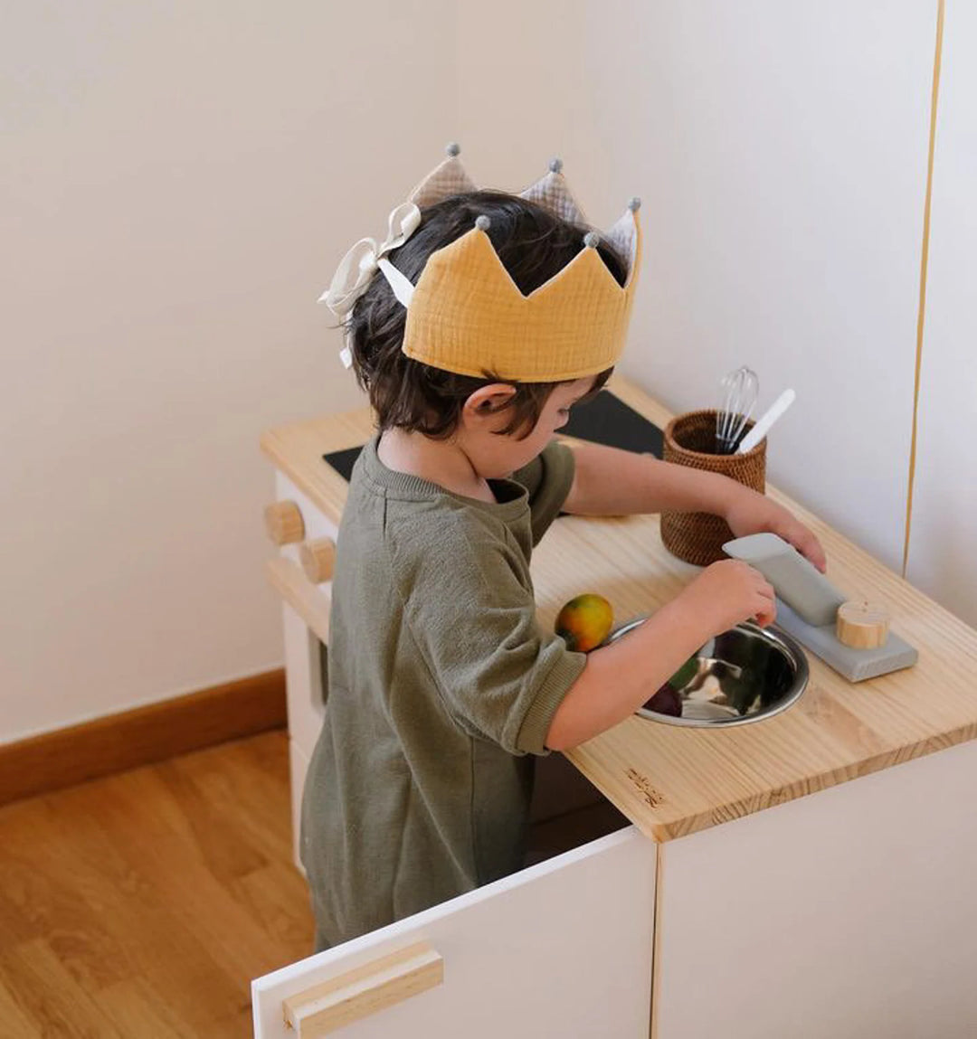 Enfants qui joue dans une cuisine avec Couronne réversible en tissu jaune et écru avec pompons gris