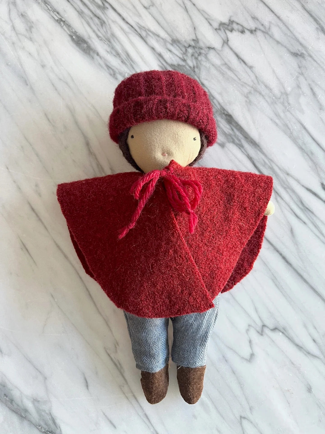 Mini poupée en laine et coton avec cape hivernal rouge, bonnet rouge, jumper bleu et bottes brunes