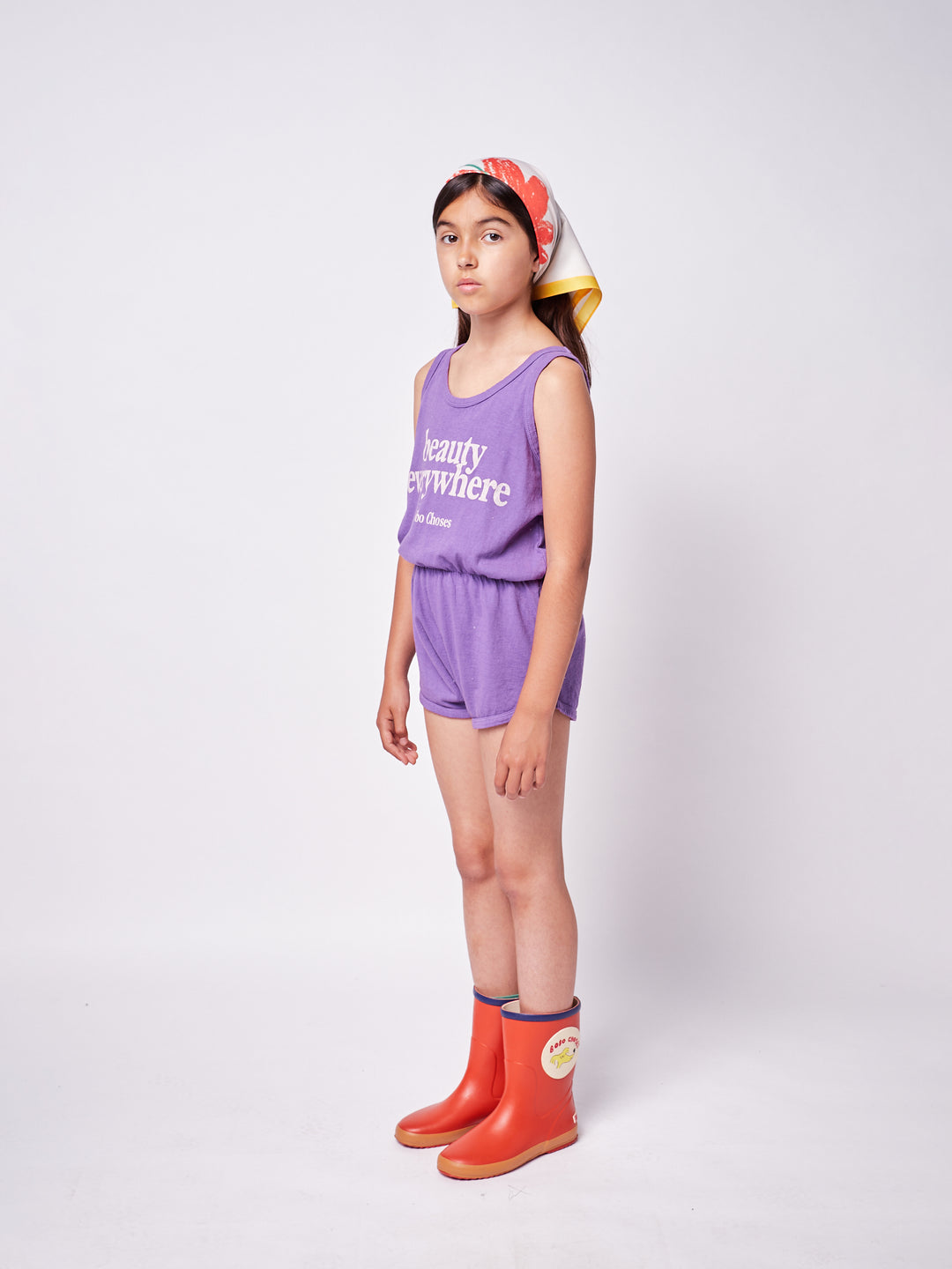brown-haired little girl with purple bobo choses ''Beauty Everywhere'' playsuit, colorful headscarf and red rainboots
