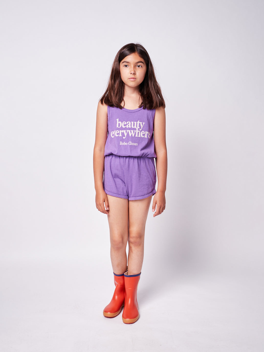 brown-haired little girl with purple bobo choses ''Beauty Everywhere'' playsuit and red rainboots