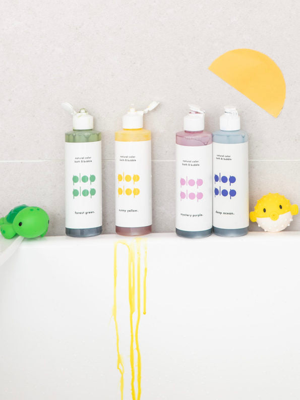 bottles of plop plop colored bubble bath by nahthing project on the side of a bathtub 